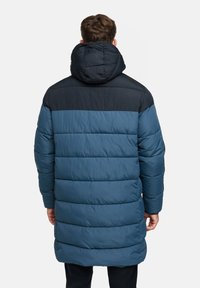 Gepolsterter Mantel in Dunkelblau und Petrol, mit abnehmbarem Kapuzen, horizontal gestepptem Design und langer Silhouette, geeignet für kältere Wetterbedingungen.