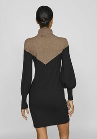 Abito in maglia caratterizzato da un corpo nero e un motivo a chevron marrone nella parte superiore. Maniche lunghe con polsini a costine. Design con collo alto.