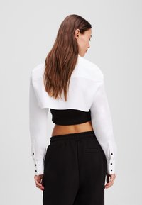 Cropped black top paired with a white long-sleeve shirt. The shirt features buttoned cuffs and a relaxed fit, highlighting contrasting colors.