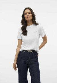 T-shirt en coton blanc à manches courtes et encolure ronde, associée à un jean en denim foncé, avec une ceinture noire à boucle dorée.