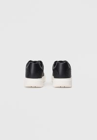 Μαύρα αθλητικά παπούτσια με υφή στην πίσω πάνελ, λείο μαύρο τακούνι και λευκή καουτσούκ σόλα. Περιλαμβάνουν ελάχιστη σήμανση στο τακούνι.