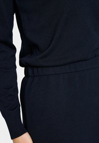 Pull en tricot navy à manches longues, avec une coupe décontractée et une taille élastique. Texture lisse, design simple, détails minimalistes.