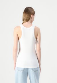 Hvit ribbet tanktop med rund halsutskjæring, ermeløs snitt og slim fit, kombinert med lyseblå løstsittende jeans.