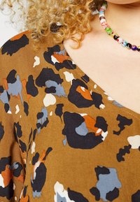 Tissu à motif floral marron avec diverses formes dans des nuances de bleu, noir et orange ; présente un col en V et une texture douce.