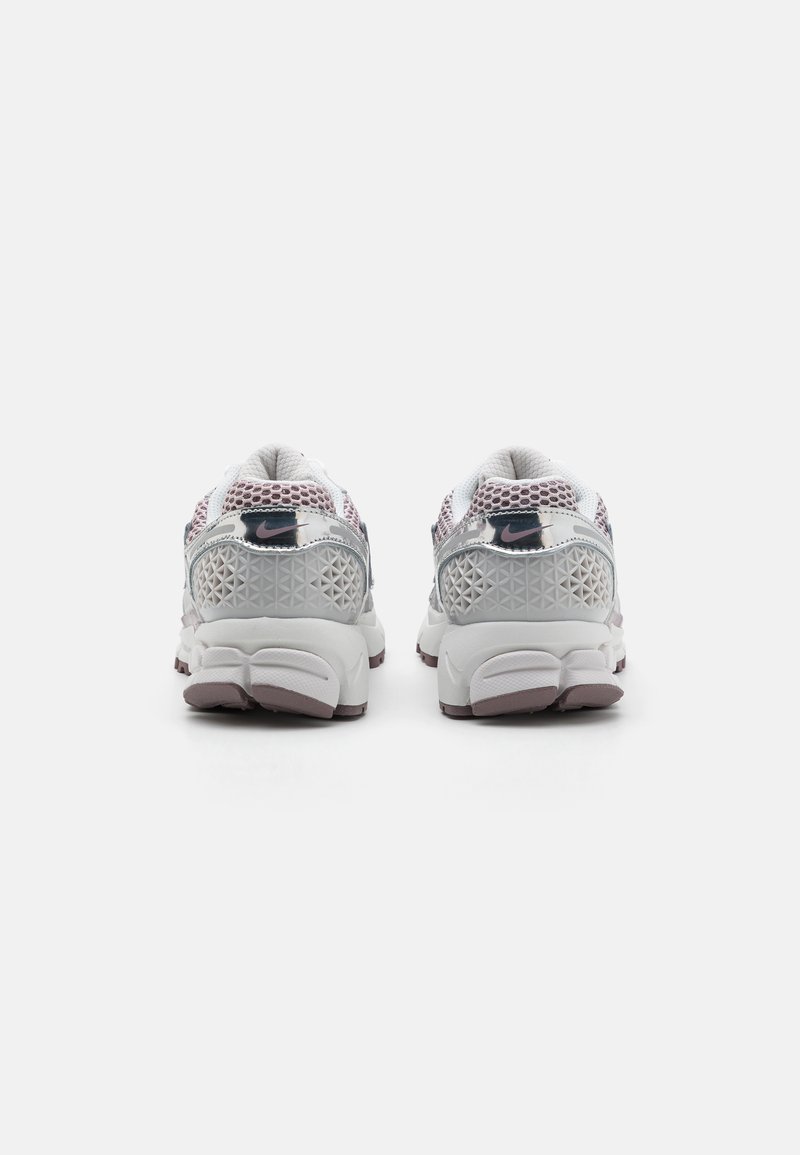 Des chaussures de sport blanches et roses présentent un dessus en maille avec des motifs géométriques, un col rembourré et une semelle en caoutchouc épaisse offrant une adhérence texturée.