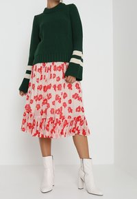 Maglione verde a coste con strisce bianche, gonna midi rosa floreale con bordo a volant e stivaletti bianchi con zip alla caviglia.