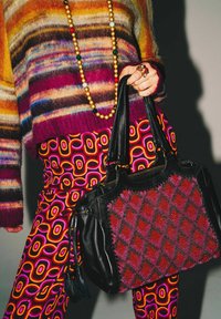 Sac à main en cuir noir avec un motif de diamants rouges et roses, assorti à un pull rayé multicolore et un pantalon à motifs.