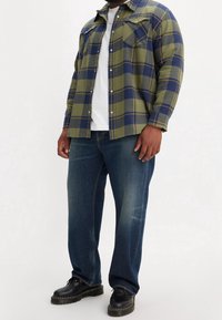 Grön och marinblå rutig flanellskjorta, vit t-shirt under, kombinerad med blåa denimjeans och svarta snörskor. Långa ärmar, två bröstfickor.