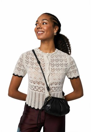 Lace-knit cream short-sleeve top with scalloped edges and button closure, paired with a black crossbody bag and maroon pants.