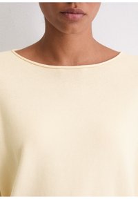 Cremefarbene Bluse mit weicher Textur und weitem, rundem Ausschnitt. Der Stoff wirkt leicht und atmungsaktiv, ideal für den Freizeitlook.