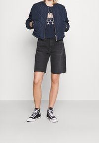 Námořnická prošívaná bomber bunda přes černé tričko s potiskem, doplněná o potrhané černé džíny a černé tenisky s vysokým kotníkem.