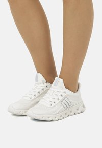 Scarpe sportive bianche con tomaia in rete testurizzata, colletto imbottito e accenti riflettenti argentati. Presentano una suola spessa e ammortizzata per il massimo comfort.
