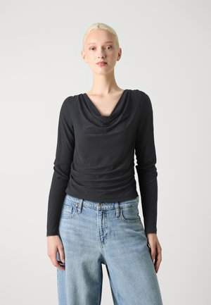 Black long-sleeve top with a cowl neckline and gathered detail at the waist, paired with high-waisted light blue jeans.