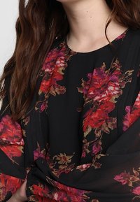 Blusa nera con grandi motivi floreali rossi e viola, con vita arricciata e lunghe maniche fluide. Tessuto morbido e leggero.