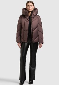 Pruun puffer-jope kõrge krae ja ševroonmustriga. Kombineeritud mustade nahksete pükste ja pahkluu saapadega.