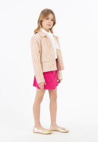 Giacca in tessuto a righe rosa e crema, dal design corto. Abbinata a una camicetta bianca e una gonna rosa brillante, completata da ballerine dorate.