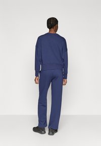 Granatowy komplet dresowy z miękkiej tkaniny; bluza z opuszczanymi ramionami i prążkowanym dołem; spodnie o wąskim kroju z elastycznym pasem.