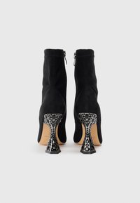 Bocanci scurți din suede negru cu toc metalic decorativ, având un design texturat unic și fermoare laterale pentru o îmbrăcare ușoară.