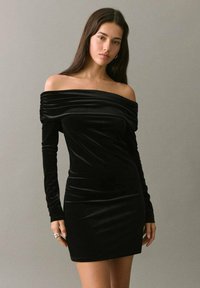 Rochie neagră din catifea, cu umerii descoperiți, mâneci lungi și detalii pliate în jurul gâtului, siluetă ajustată și textură fină.