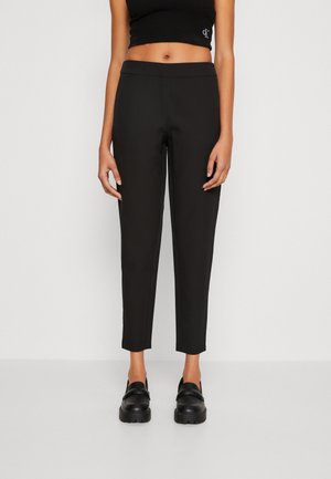 Zwarte rechttoe-rechtaan broek van een gladde stof, met een middelhoge taille en enkel lengte. Gecombineerd met zwarte instappers, die een minimalistisch ontwerp bieden.
