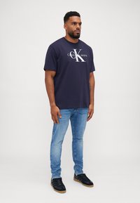 Camiseta de algodón azul marino con el logotipo blanco de "Calvin Klein Jeans". Combinada con unos vaqueros de mezclilla azul claro y zapatillas negras.