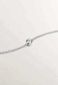 Pulsera de cadena de plata con una gema clara redonda montada en un bisel pulido en el centro. Textura suave, diseño sencillo.