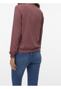 Wijnrode trui met een geribde zoom en manchetten, gemaakt van gladde stof. Gecombineerd met blauwe spijkerbroeken met een standaard ontwerp van de achterzak.