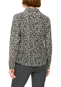 Woman wearing a long-sleeve black and white floral patterned blouse and dark gray pants, shown from the back against a white background.