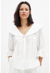 Blusa bianca in cotone con un ampio colletto, chiusura a bottoni sul davanti e maniche a sbuffo. Presenta motivi a occhiello e bordi scallop.