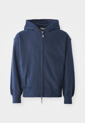 Mørkeblå zip-up hettegenser laget av mykt stoff, med snøring på hetta, ribbede mansjetter og sidelommer. Enkelt design med minimal merkevare.