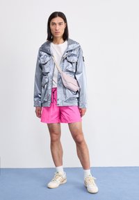 Silver reflective jacket with multiple pockets, pink shorts, white T-shirt, and cream sneakers. Crossbody bag in light pink.