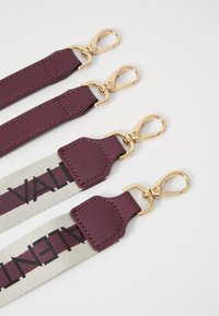 Cinghie regolabili per borse in un ricco color burgundy e tela con stampa del logo. Gli accessori in metallo dorato e gli accenti testurizzati migliorano la durata e lo stile.