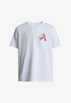 Valge lühikeste varrukatega T-särk, millel on vasakul rindkerel punane täht "A" ja valge lillemuster.