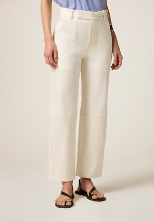 Crème wijde broek met hoge taille, voorzakken, platte naden en een soepele stof, gecombineerd met zwarte sandalen.