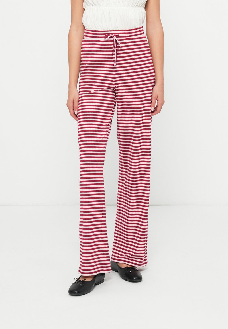 Calças listradas em vermelho e branco com cintura elástica, design evasé e tecido texturizado, combinadas com sapatos planos pretos.