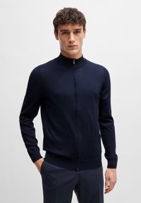 Navy zip-up cardigan made of soft fabric, featuring a high neckline, long sleeves, and a fitted waist. Lightweight design with smooth texture.