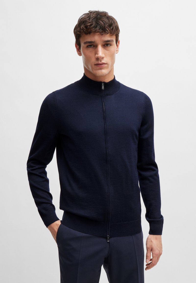 Navy zip-up cardigan made of soft fabric, featuring a high neckline, long sleeves, and a fitted waist. Lightweight design with smooth texture.
