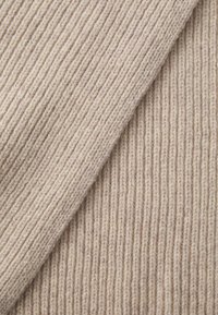 Beige ribbestrikket stoff med en myk, teksturert overflate. Har vekslende tykke og tynne vertikale linjer. Lett og fleksibelt materiale.