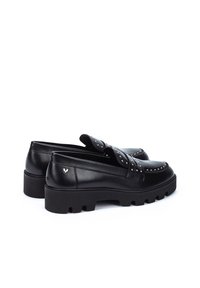 Mocasines de cuero negro con acentos de tachuelas, suela de goma gruesa y textura lisa. Presentan un logo en el talón y un diseño fácil de poner.