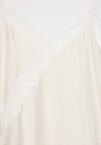 Kremasto satensko oblačilo z nežno belo čipko ob vratu in diagonalnem šivu ter tankimi čipkastimi naramnicami.