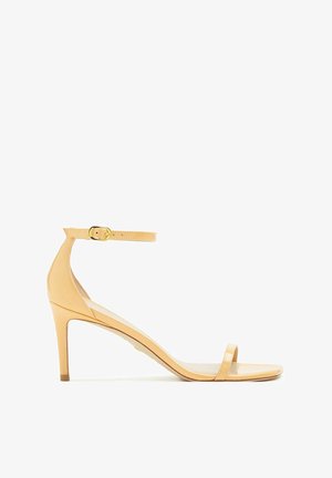 Sandale à talons hauts beige avec des brides et une fine lanière à la cheville, bout ouvert. Fabriquée dans un matériau brillant avec une texture lisse et un minimum de détails.