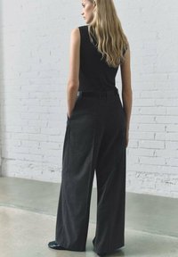 Pantalon ample gris en tissu texturé, doté d'une taille haute, de passants de ceinture et de poches latérales. Associé à un haut noir ajusté.