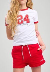 T-shirt blanc avec des bordures rouges arborant le numéro "24" et "New York City" en noir. Short rouge avec cordon de serrage et texte brodé.