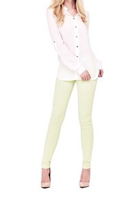 Chemise blanche à boutons, à manches longues et boutons noirs, associée à un jean slim vert clair et des chaussures à talons nus.