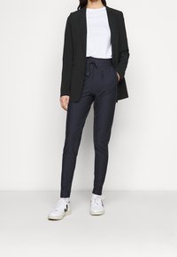 Marinblå randiga byxor med elastisk midja, kombinerat med en vit t-shirt och en svart kavaj. Vita sneakers fulländar outfiten.