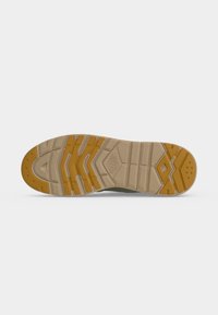Semelle de chaussure avec des crampons en caoutchouc beige et jaune moutarde présentant des motifs géométriques et des rainures pour l'adhérence sur fond blanc.