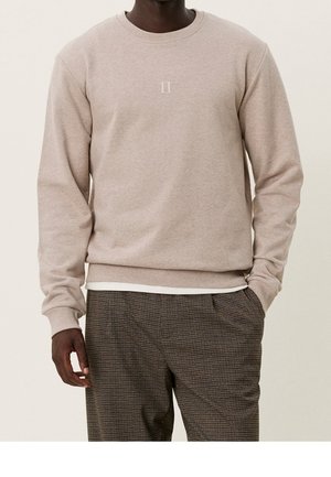 Sudadera de color beige claro con un cuello redondo y un sutil logo "II" en el centro. Fabricada en tejido suave, combinada con pantalones marrones con estampado.