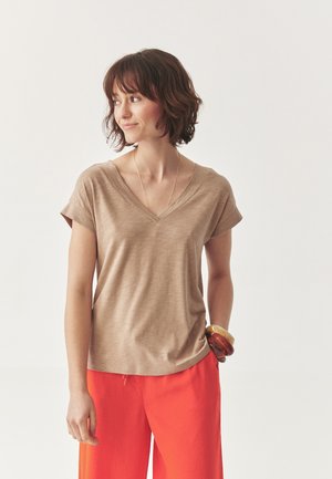 Beige V-hals t-shirt met opgerolde korte mouwen, gecombineerd met feloranje wijde broekspijpen. De stof lijkt zacht en lichtjes gestructureerd.