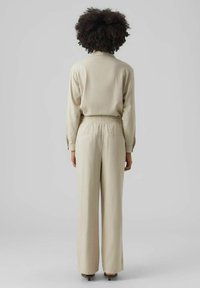 Haut beige à manches longues avec une coupe décontractée, associé à un pantalon large taille haute. Texture lisse avec une taille élastique.