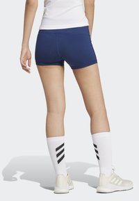 Shorts sportivi blu navy con una texture liscia, caratterizzati da un taglio a vita bassa e un design aderente. Abbinati a calze bianche al ginocchio con strisce nere.